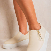 Beige slip-on trainers with side zipper detail and gold-tone accents on platform sole