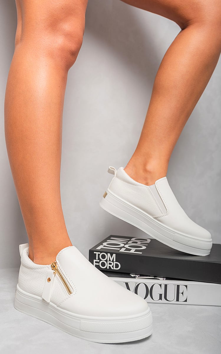 White slip-on trainers with side zipper detail and gold-tone accents on low profile sole