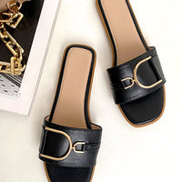 Black slide sandals with wide straps and gold-tone ring detail, front angle