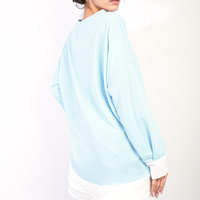 Sky blue long-sleeve oversized dress top with contrast ruffle hem, back/side view