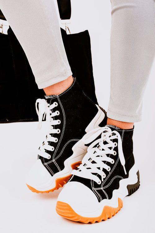 Black high-top platform trainers with white laces, white panels, and orange sole