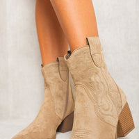 Beige ankle boots with western-style stitching, pull tab, and stacked wooden heel