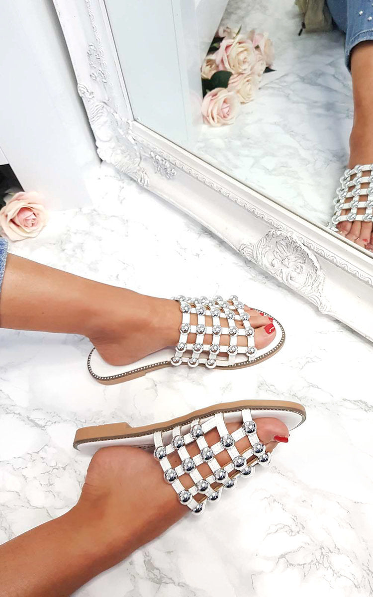 Studded lattice flat slide sandals on floor, jeweled straps and tan sole in pair