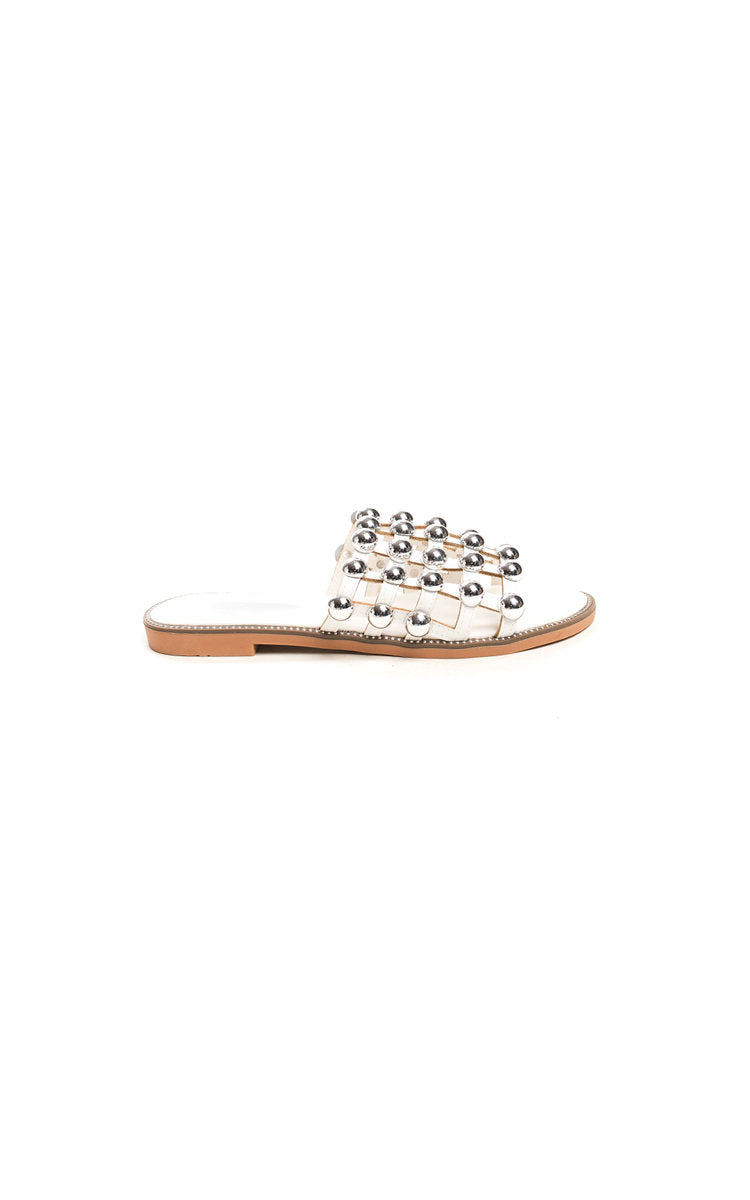 White flat slide sandals with silver studded lattice strap over the toe