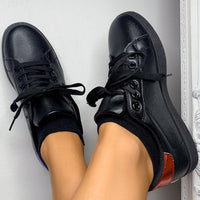 Black lace-up trainers on feet, with orange-red side stripe and white sole