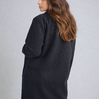 Dark textured button-front long jacket with front pockets and three-quarter sleeves.