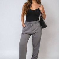 Grey high-waist drawstring trousers with side pockets and gathered waistband.
