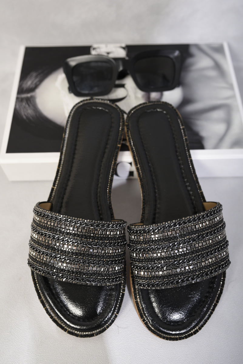 Black flat slide sandals with wide rhinestone straps and glossy black footbed