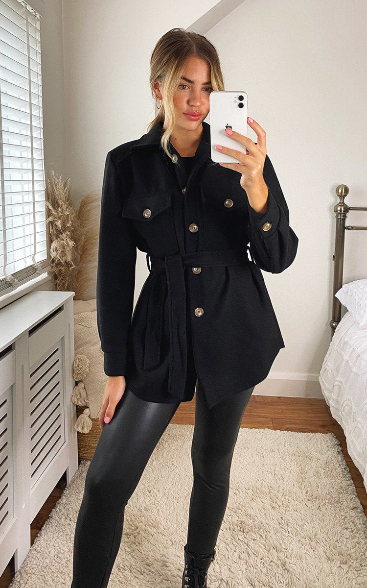 Black belted jacket with button front, flap pockets, and long sleeves in a fitted waist.