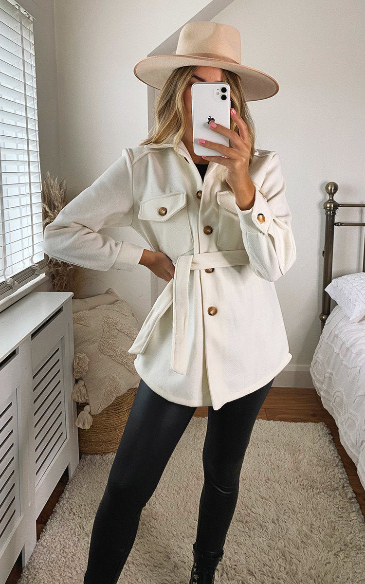 White belted jacket with flap pockets, gold buttons, and tie waist detail.