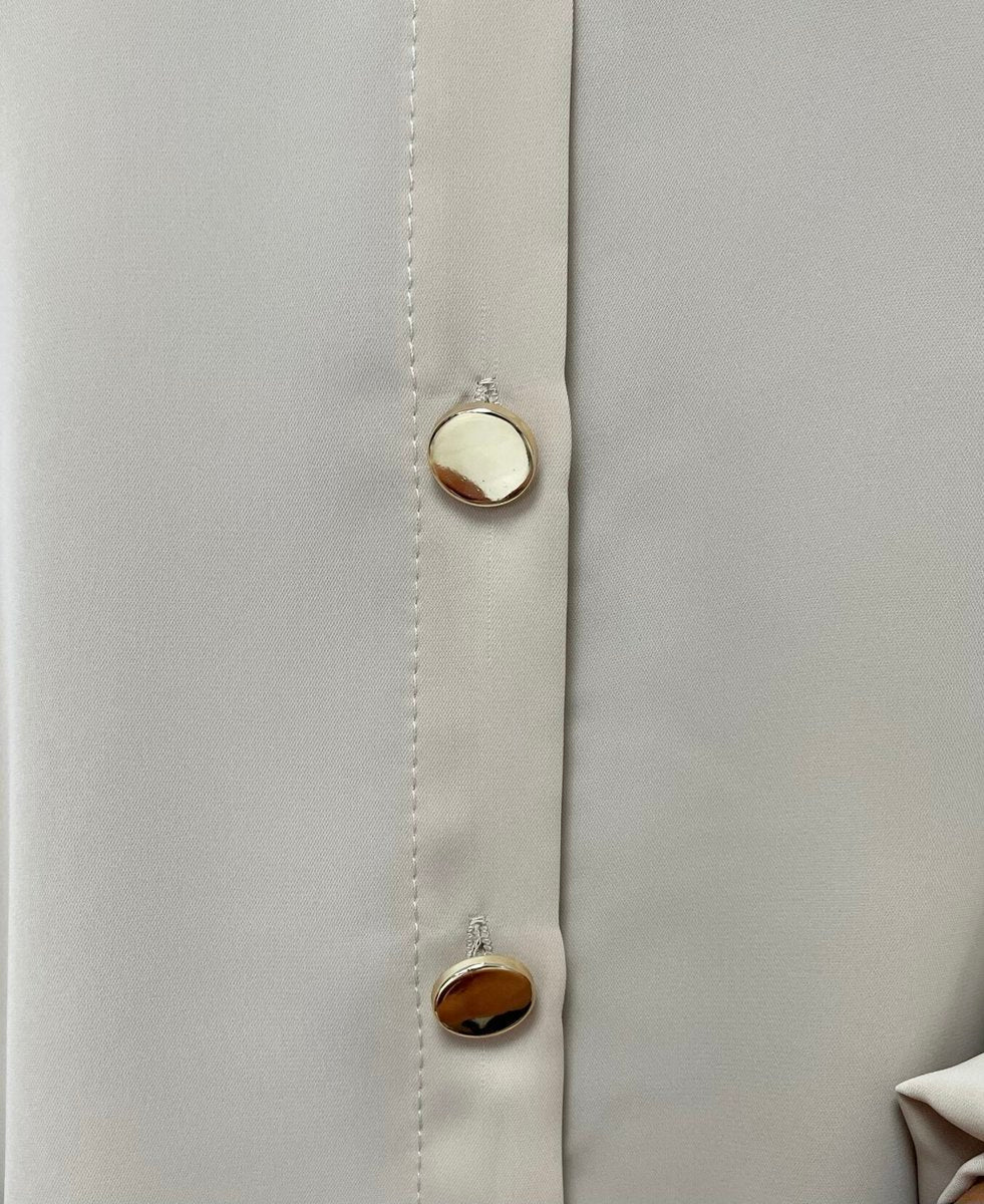 Beige button placket close-up with round gold-tone buttons and vertical stitching