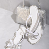 White flat thong sandals with jeweled bow and silver-trimmed edges