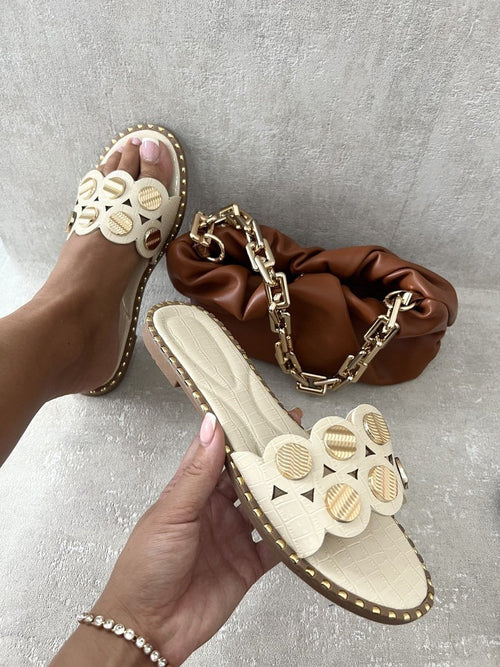 Beige flat sandals with studded trim, circular cutout straps, and open toe