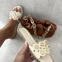 Beige flat sandals with studded trim, circular cutout straps, and open toe