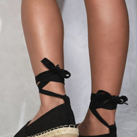 Black espadrilles with crisscross ankle ties and woven toe caps, casual low wedge