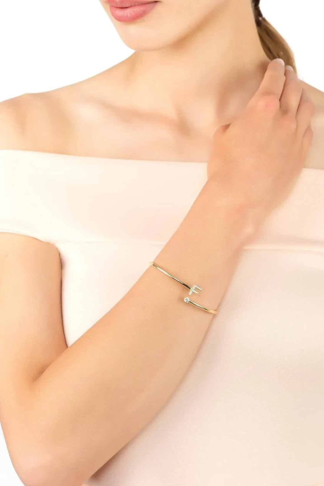 Gold initial F bangle bracelet on wrist with crystal cross and small stones