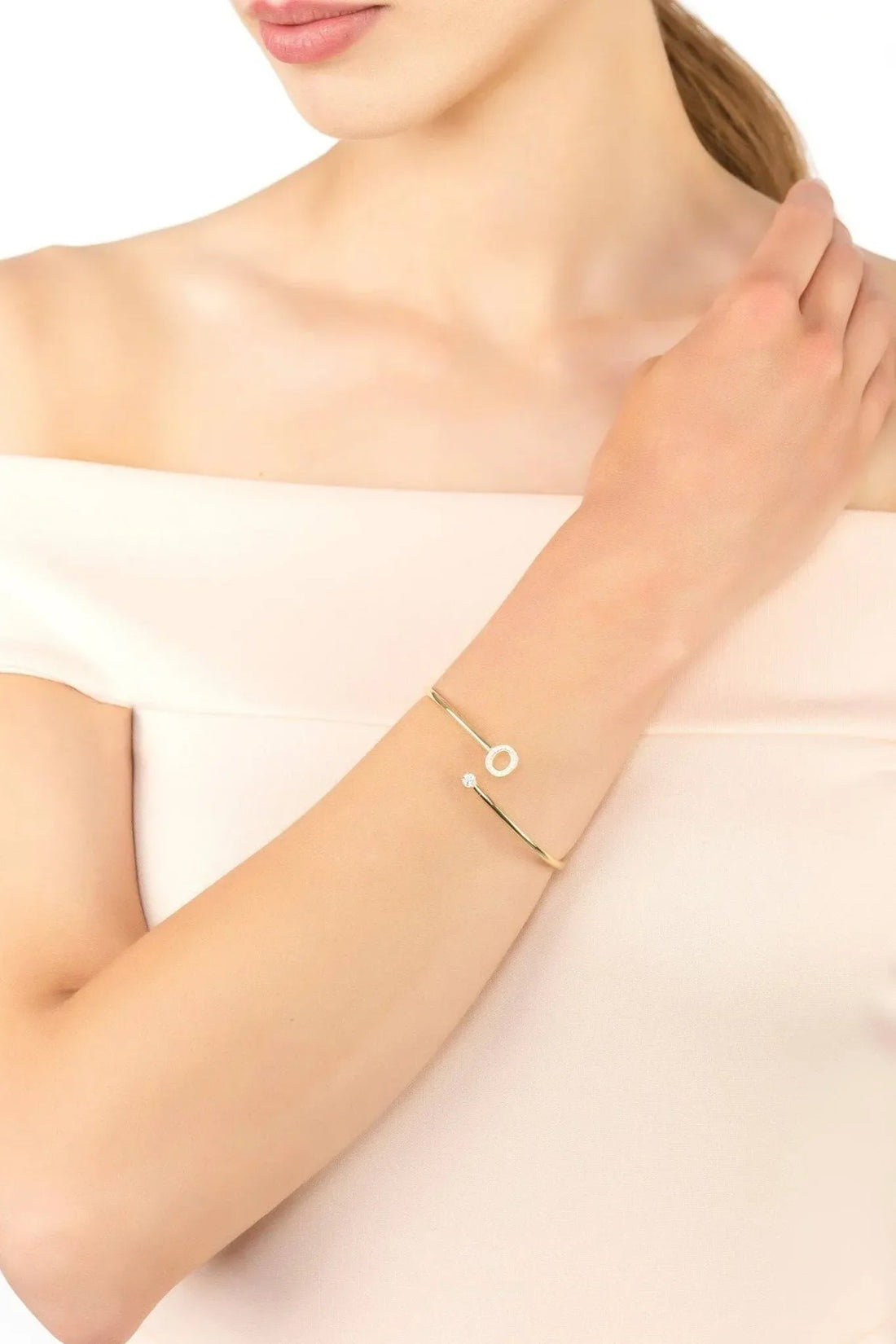 Gold-tone initial bangle with O charm worn on wrist with small stone detail