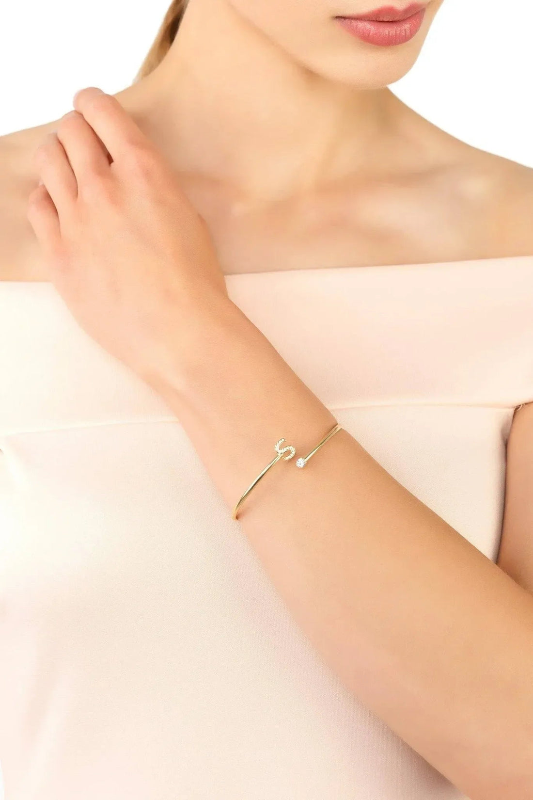 Gold-tone initial S bangle worn on wrist with small crystal accents