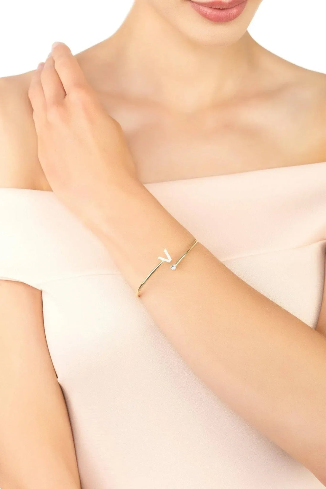 Gold-tone V initial bangle on wrist with small crystal details