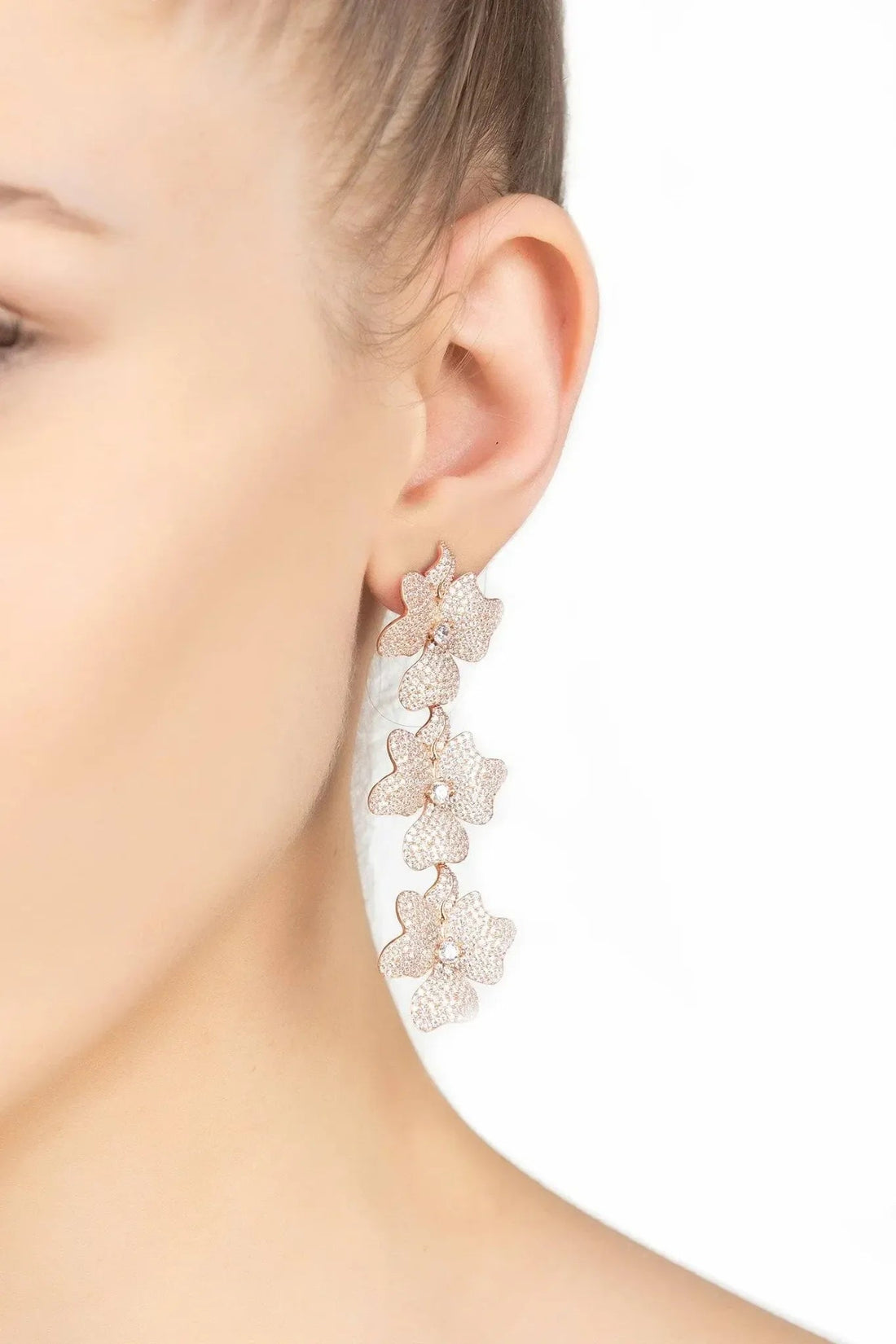 Rose gold triple flower drop earrings on the ear, sparkly textured blossoms.