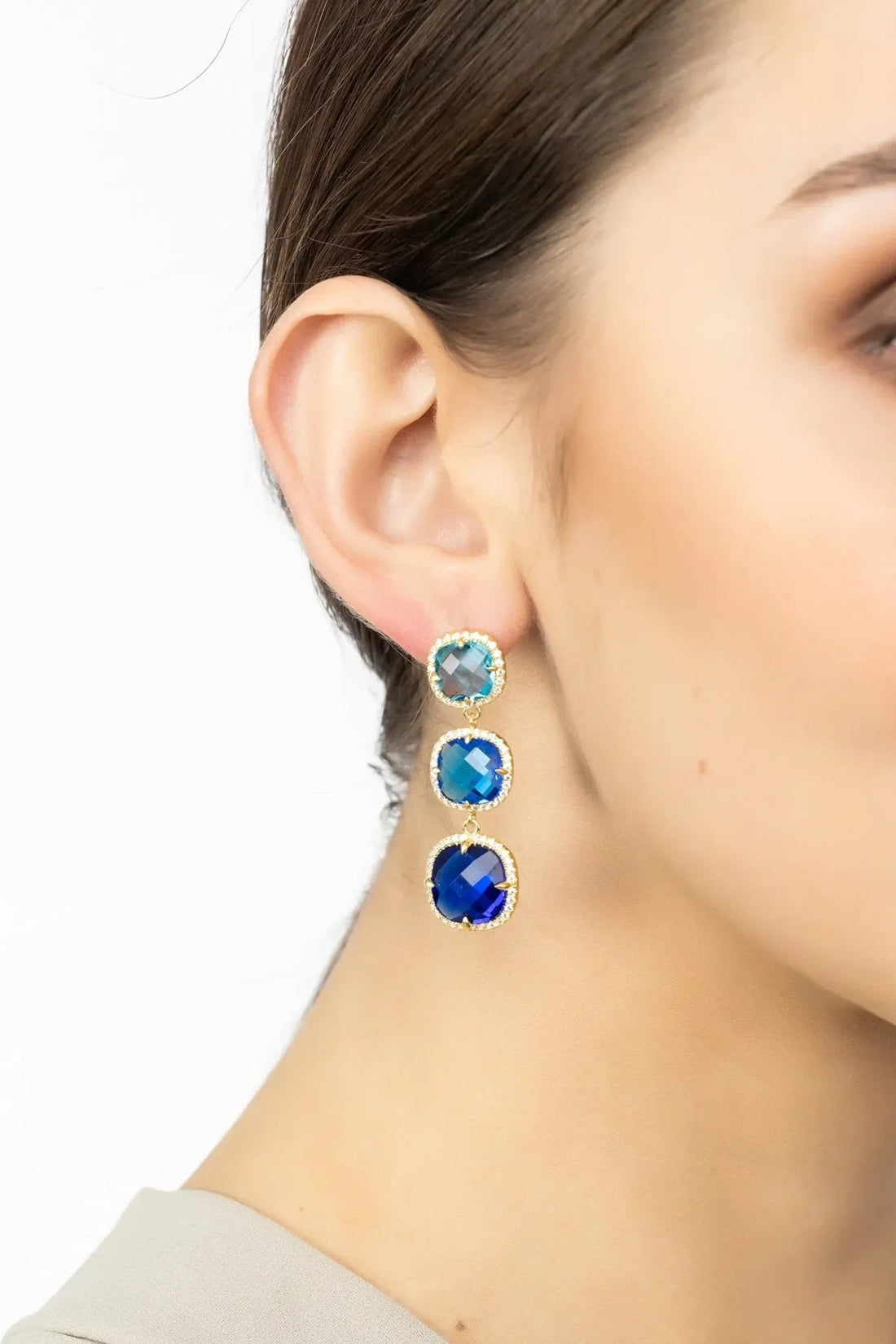 Blue and gold drop earrings shown on ear with three faceted stone tiers