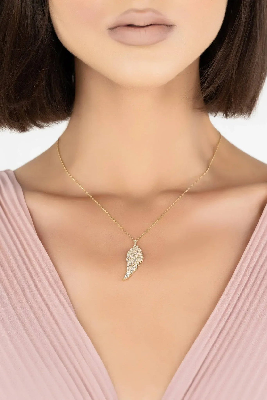 Gold angel wing pendant necklace on neckline with thin chain and wing charm
