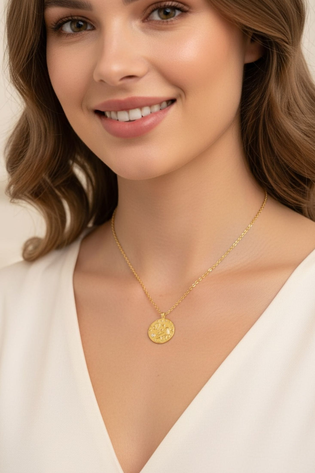 Gold-tone necklace with round Leo zodiac pendant, worn on V-neck white top