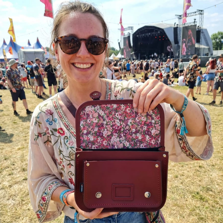 Oxblood leather satchel with gold hardware and floral-lined interior, held by model