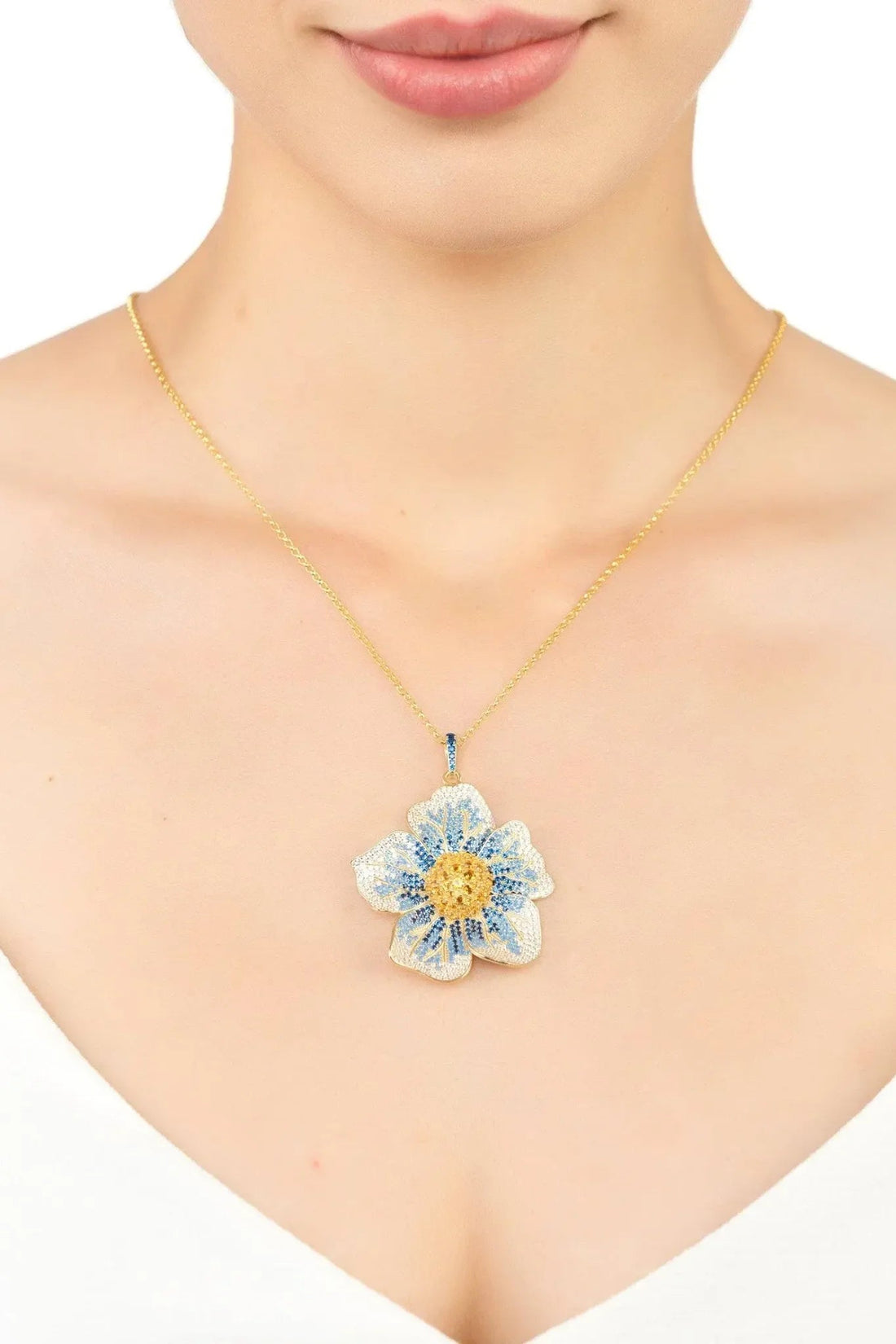 Gold necklace with blue flower pendant worn at the collarbone