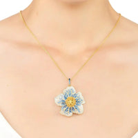 Gold necklace with blue flower pendant worn at the collarbone