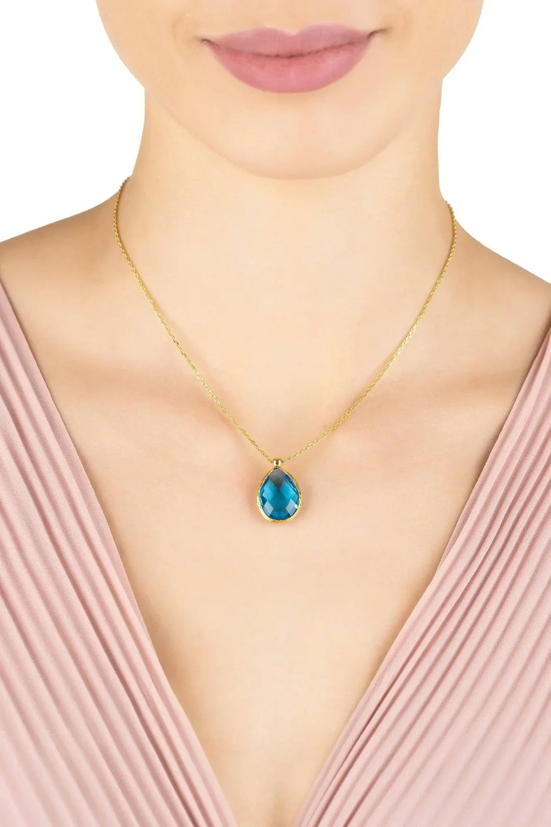 Gold necklace with blue topaz teardrop pendant worn at the neckline