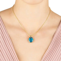 Gold necklace with blue topaz teardrop pendant worn at the neckline
