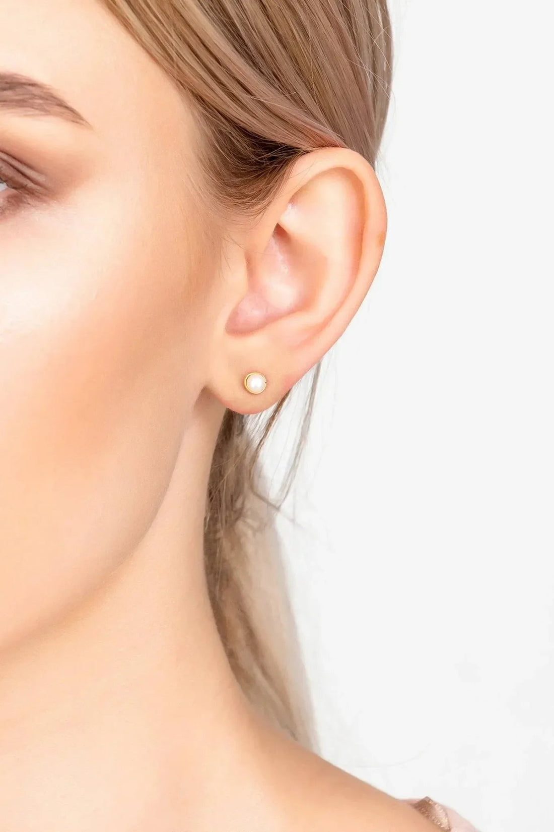 Small gold-tone pearl stud earrings on side profile ear