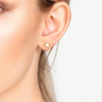 Small gold-tone pearl stud earrings on side profile ear