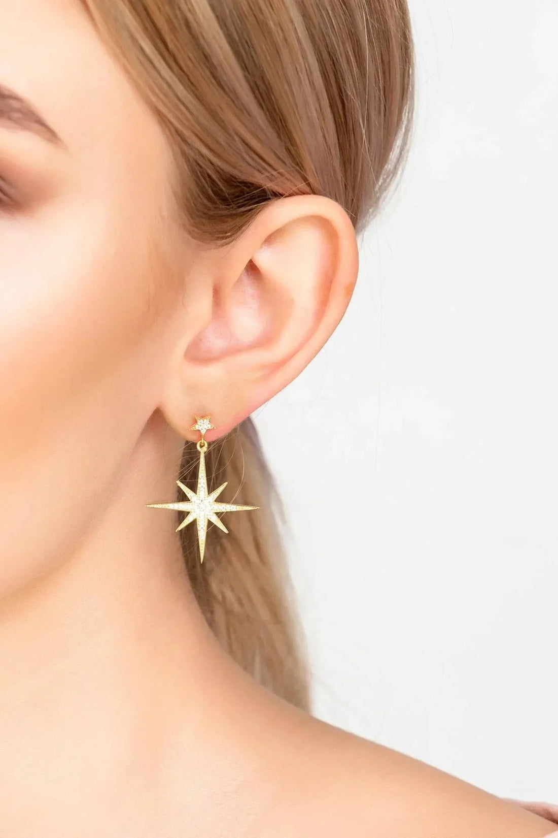 Gold starburst drop earrings with dangling star charm, shown on ear