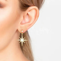 Gold starburst drop earrings with dangling star charm, shown on ear