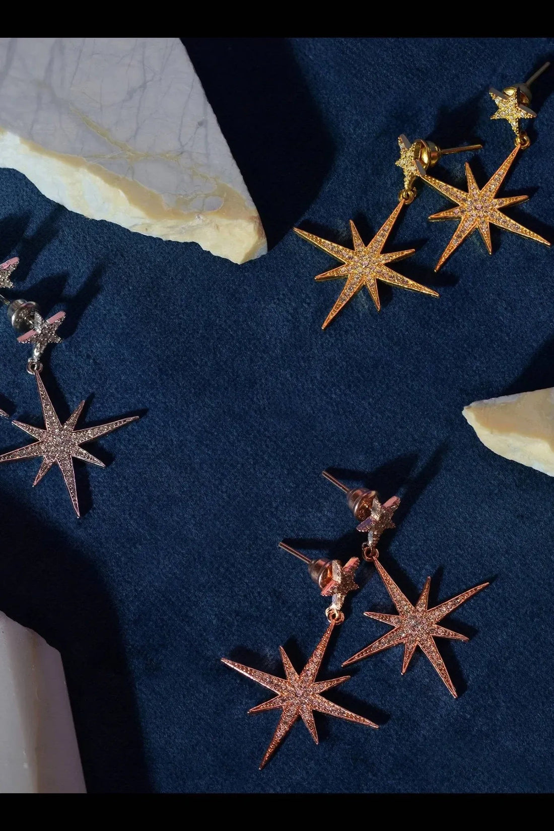 Gold starburst drop earrings with dangling star charms laid on fabric