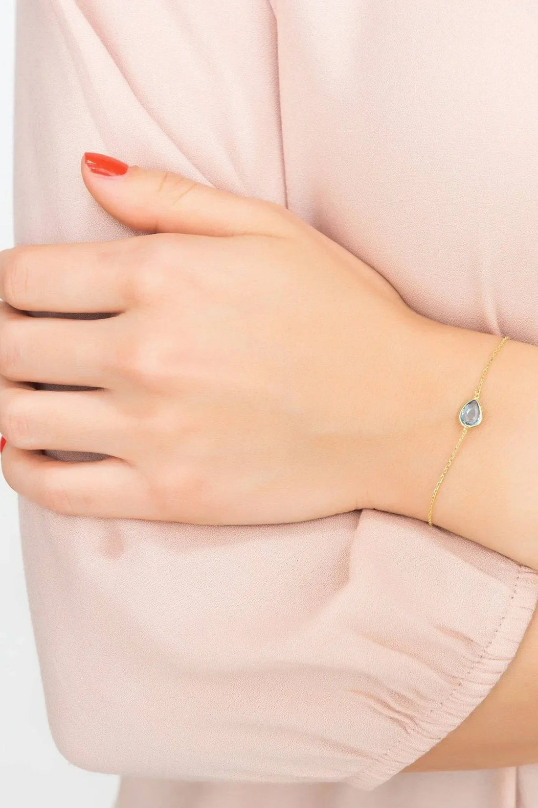 Gold bracelet with blue teardrop stone on wrist, thin linked chain