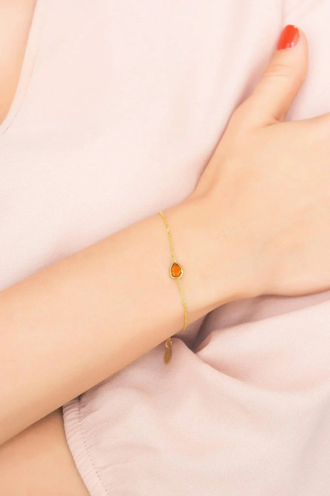 Gold mini teardrop bracelet on wrist with orange teardrop stone