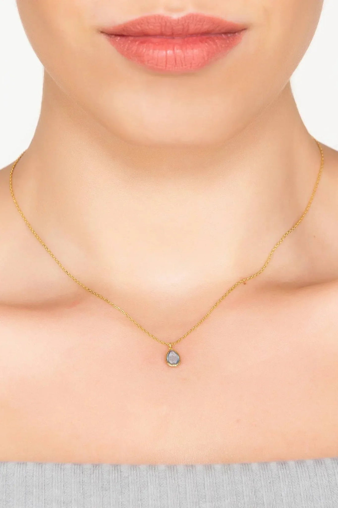 Gold teardrop pendant necklace with blue stone, worn at collar