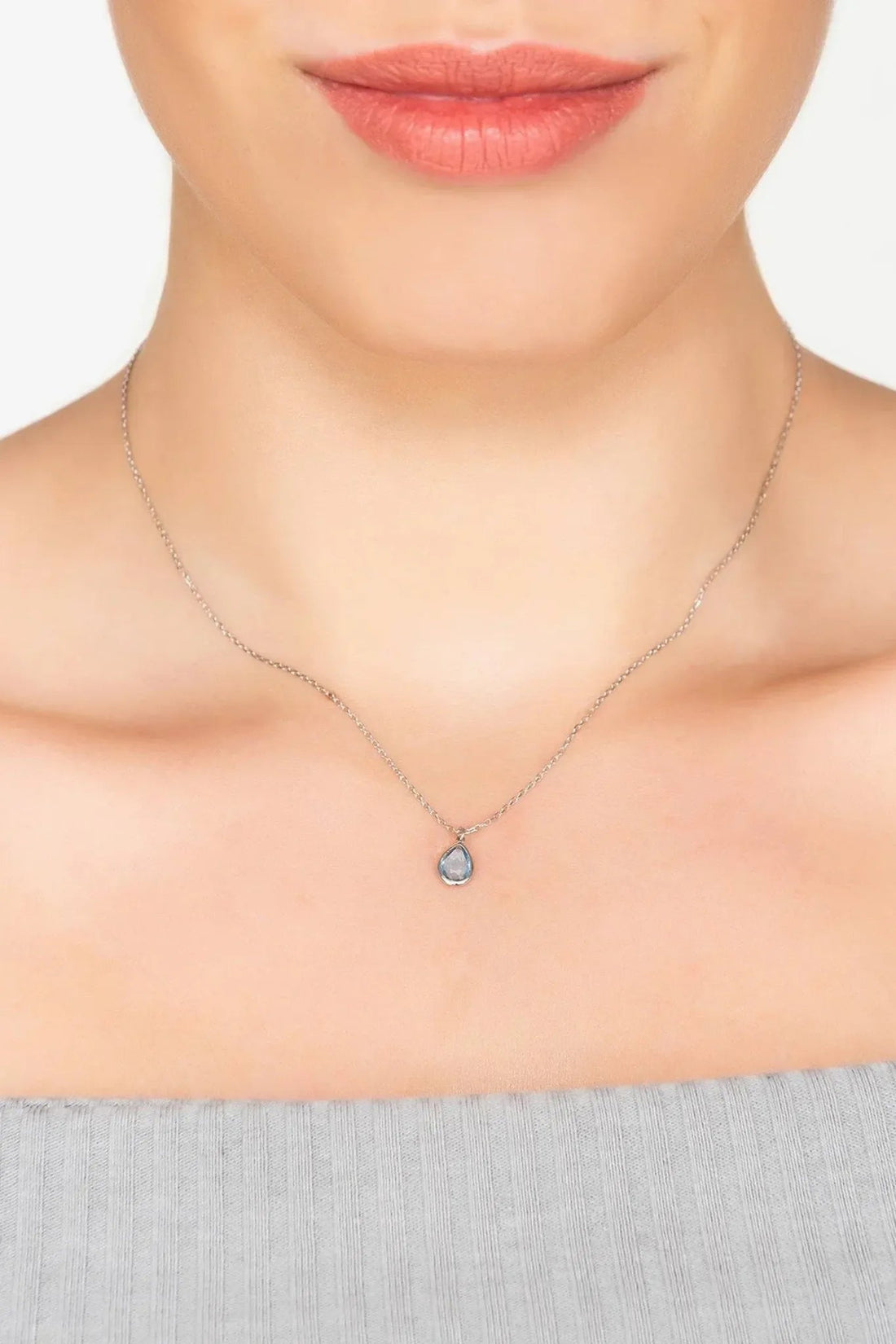 Silver teardrop pendant necklace with light blue topaz worn at the neckline