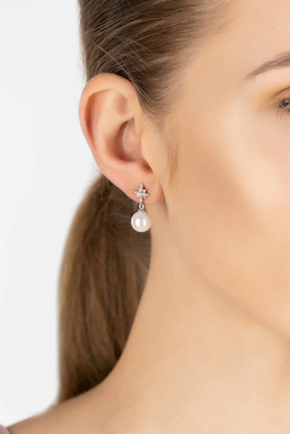 Silver star and pearl drop earrings on model ear, side view