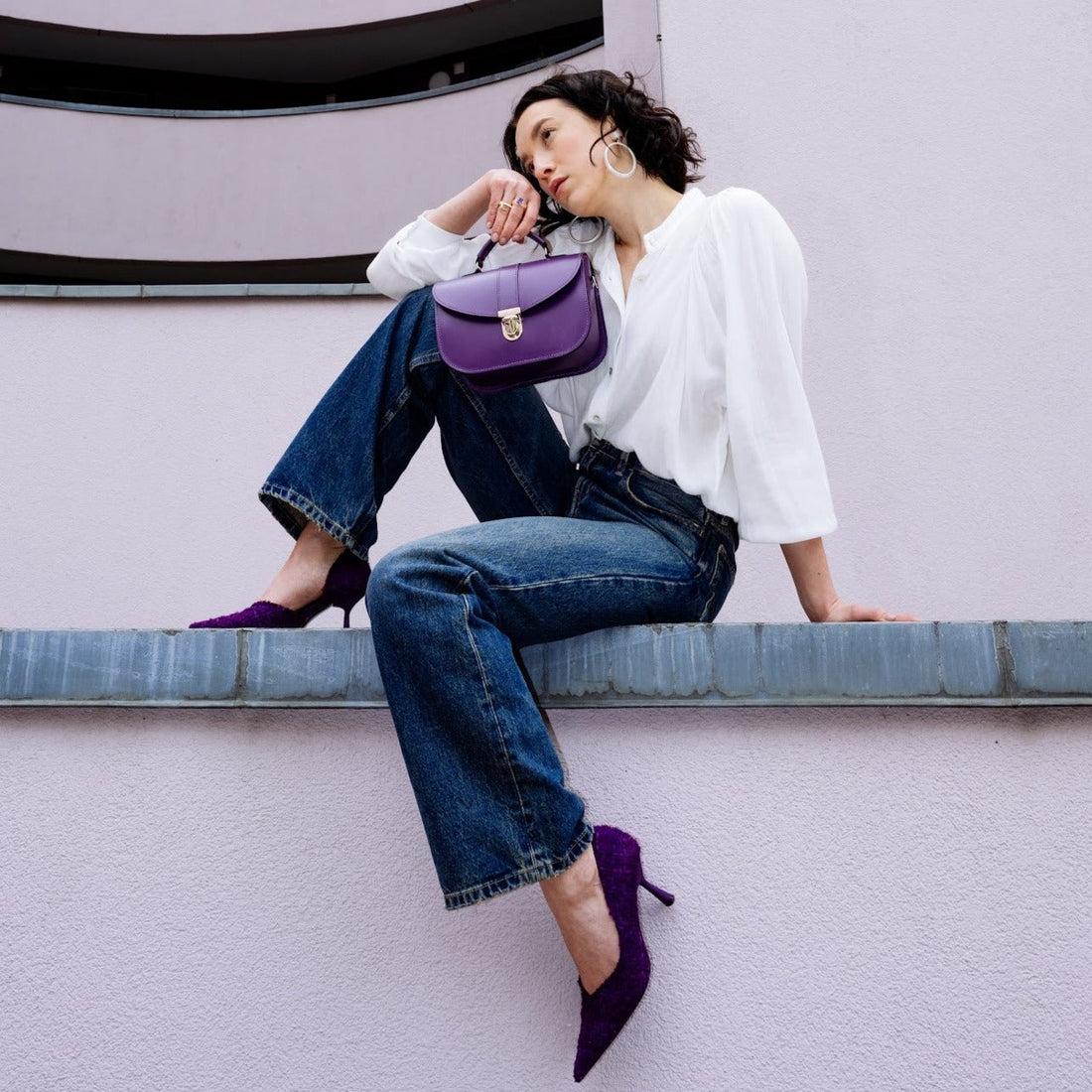 Purple leather flap crossbody bag worn with adjustable shoulder strap