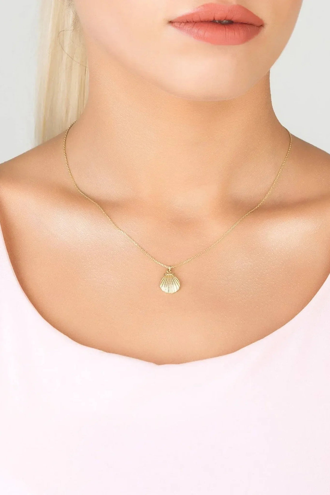 Gold shell pendant necklace with thin chain worn at the collarbone