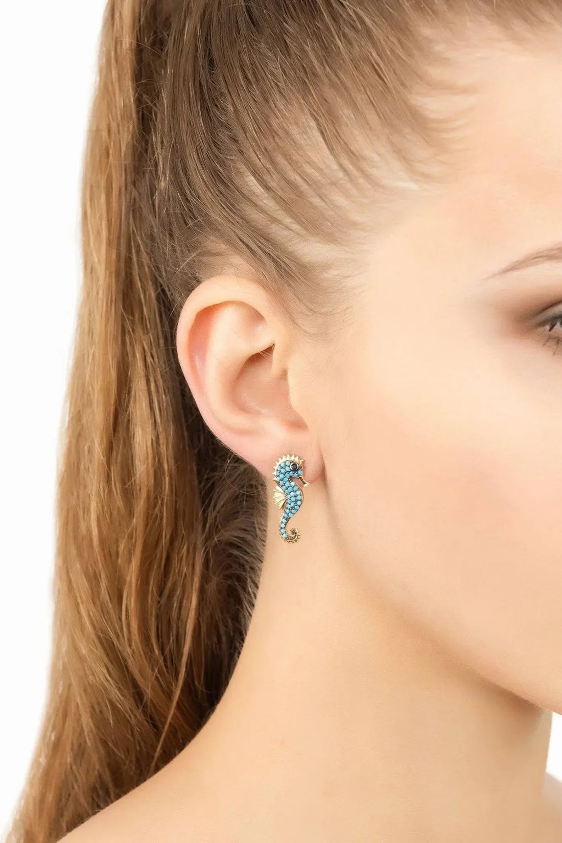 Turquoise seahorse stud earrings with gold-tone details on an ear