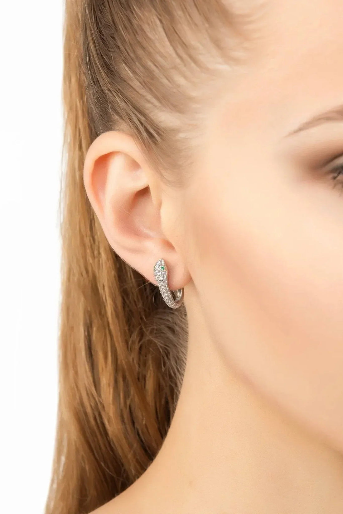 Silver snake huggie hoop earrings on ear with green enamel and clear stones
