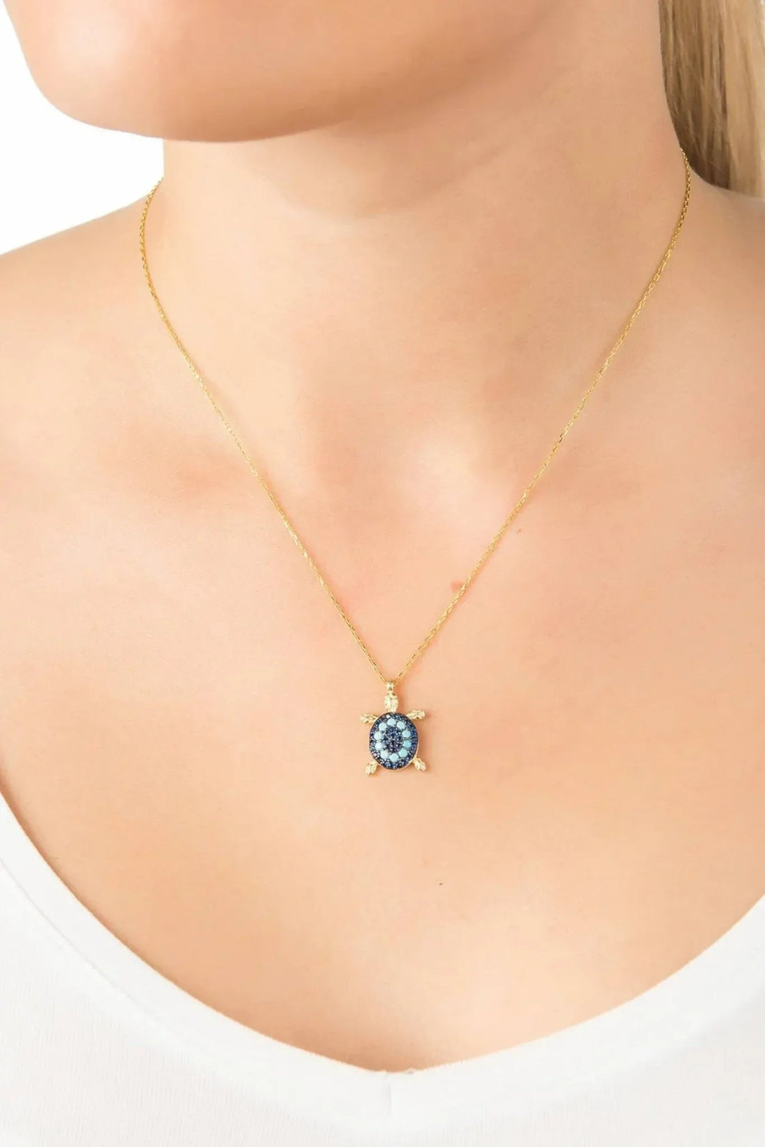 Gold-tone pendant necklace worn at neckline, blue turtle charm with turquoise stones