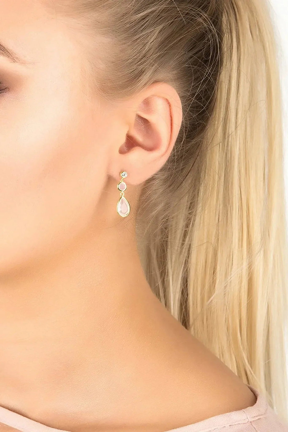 Gold-tone drop earrings with pale pink teardrop gemstone on ear