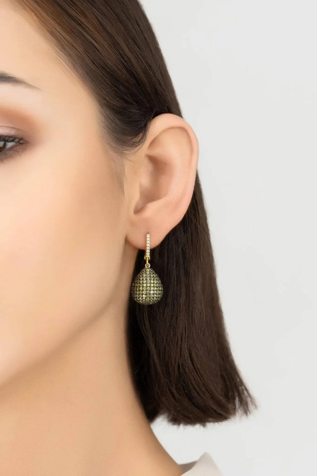Gold teardrop dangle earrings with textured green gemstone drops, worn on ear