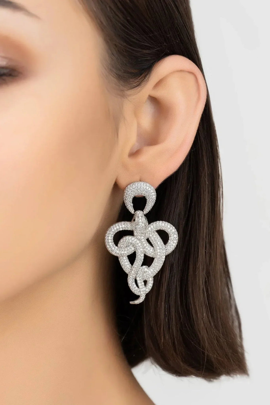 Silver rhinestone drop earrings with braided knot design on model&